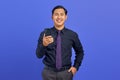 Cheerful young handsome businessman holding smartphone and looking at camera on purple background Royalty Free Stock Photo