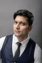 A cheerful, young, handsome Indian male model in formal wear wearing white shirt, black tie, black coat against grey background. Royalty Free Stock Photo