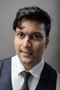 A cheerful, young, handsome Indian male model in formal wear wearing white shirt, black tie, black coat against grey background. Royalty Free Stock Photo