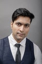 A cheerful, young, handsome Indian male model in formal wear wearing white shirt, black tie, black coat against grey background. Royalty Free Stock Photo