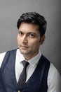 A cheerful, young, handsome Indian male model in formal wear wearing white shirt, black tie, black coat against grey background. Royalty Free Stock Photo