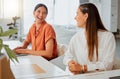 Cheerful young hispanic business woman working on a laptop while talking to a colleague in an office. Two happy Royalty Free Stock Photo