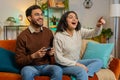 Cheerful young Indian family couple using joystick controller playing video game fun sitting on sofa Royalty Free Stock Photo