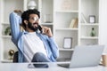 Cheerful Young Indian Guy Talking On Cellphone While Working In Home Office Royalty Free Stock Photo