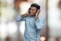 Cheerful young indian man listening music with headphones. Interior blur background. Royalty Free Stock Photo