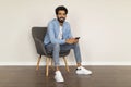 Cheerful Young Indian Man With Smartphone In Hands Relaxing In Armchair Indoors Royalty Free Stock Photo