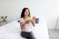 Cheerful young Indian woman eating yummy vegetable salad while sitting on bed at home, copy space Royalty Free Stock Photo