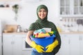 Cheerful young islamic housewife holding bucket with cleaning supplies Royalty Free Stock Photo