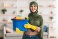 Cheerful young islamic housewife holding bucket with cleaning supplies tools Royalty Free Stock Photo