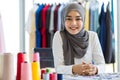 Cheerful young Islamic woman designer in traditional headscarf sitting at table in atelier workshop smiling at camera. Concept for