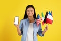 Cheerful young japanese woman student with many different flags show phone with empty screen