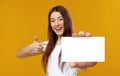 Cheerful young lady pointing at empty business card, smiling at camera on orange studio background, mockup Royalty Free Stock Photo