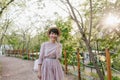 Cheerful young lady in trendy pale-purple gown walking in park and speaking with friend on cell. Portrait of joyful Royalty Free Stock Photo