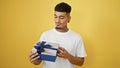 Cheerful young latin man holding a birthday present with confidence, smiling happily on a vibrant, isolated yellow background