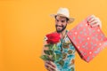 cheerful young Latino man in Hawaiian clothes holding a red rose and a gift medium shot orange background studio shot
