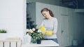 Cheerful young maid is dusting the furniture holding wet cloth and cleaning vase and table in modern light apartment Royalty Free Stock Photo