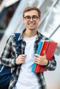 Cheerful young male student in casual outfit with bright smile holding folders while standing on the street Royalty Free Stock Photo