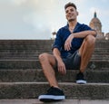 Cheerful young man in casual clothing sitting on the steps of a modern city building Royalty Free Stock Photo