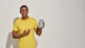 Cheerful young man in casual yellow t shirt smiling at camera, showing and pointing at smartphone with blank screen Royalty Free Stock Photo