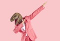 Cheerful young man in dinosaur rubber mask makes dab dance gesture isolated on pink background. Royalty Free Stock Photo