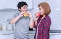 Man eating hamburger with his girlfriend holding fresh apple in her hand at home.Happy young woman dieting eat Royalty Free Stock Photo