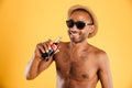 Cheerful young man in hat and sunglasses drinking coke Royalty Free Stock Photo