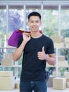 Cheerful young man holding colorful shopping bags, giving thumb up, and looking at the camera while standing in the office Royalty Free Stock Photo