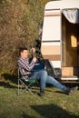 Cheerful young man playing on his guitar in front of his retro camper van
