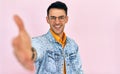 A cheerful young man raises his hand to handshake as meets someone. Male in a denim jacket and transparent spectacles pulls arm in