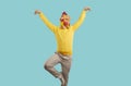 Cheerful young man in rubber rooster mask shows funny dance moves on turquoise background.