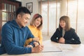 Cheerful young man signing some documents while sitting at desk together with his wife. Royalty Free Stock Photo