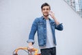 Cheerful young man talking on the mobile phone and smiling while standing near his bicycle Royalty Free Stock Photo