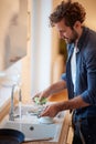 A cheerful young man washing dishes in the kitchen. Kitchen, housework, quarantin, home Royalty Free Stock Photo