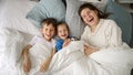 A cheerful young mother in bed with her two sons waving at the camera. This captures the essence of family happiness, spending