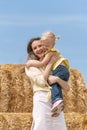 Cheerful young mother holds her little daughter in her arms against the background of haystack and blue sky. Countryside holidays Royalty Free Stock Photo