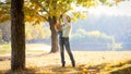 Cheerful young mother hugging her 1 year old toddler boy and showing him leaves on autumn trees at park Royalty Free Stock Photo