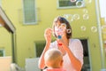 Cheerful young mother standing outdoors blowing bubbles for her