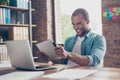 Cheerful young mulatto worker is plying a game on his tablet in office. He is very excited, wearing casual smart, funny grimace