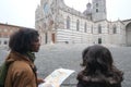 Cheerful young multiethnic couple of tourists with map visiting historical town of Siena, Italy