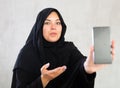 Cheerful young muslim lady in black traditional hijab showing new phone model