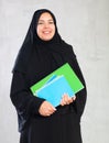 Cheerful young muslim student dressed in black hijab holding textbooks