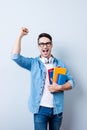 Cheerful young nerdy student is standing with books on pure back