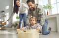 Cheerful young parents are playing with their little daughter, carrying her around house in box. Royalty Free Stock Photo