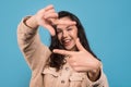 Cheerful young pretty european lady looking through fingers like camera isolated on blue background