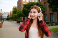 Cheerful young red haired woman posing in the street. Listen to music with headphones concept. Royalty Free Stock Photo