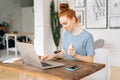 Cheerful young redhead woman is cleaning keyboard of laptop with sanitizer before starting work