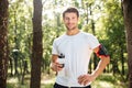 Cheerful young sportsman standing and drinking water in forest