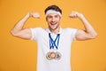 Cheerful young spotrsman with three medals showing biceps