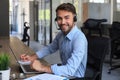 Cheerful young support phone male operator in headset, at workplace while using laptop Royalty Free Stock Photo