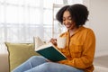 A cheerful young woman with a beautiful curly afro engages in reading a green hardcover book Royalty Free Stock Photo